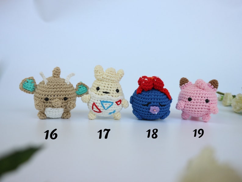 May include: Four handmade crochet figures in a row. The figures are in various colors, including tan, white, blue, and pink. Each figure has unique features, such as ears, bows, and facial expressions. Numbers 16, 17, 18, and 19 are below each figure.
