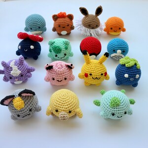May include: A collection of colorful, crocheted plush toys, each designed to resemble a different character. The toys are round and have various features, including ears, tails, and facial expressions. The color palette includes blue, yellow, orange, and purple.