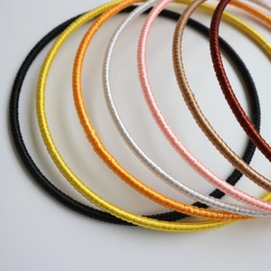 May include: A collection of colorful, thin necklaces in a variety of colors, including black, yellow, orange, silver, pink, brown, and maroon. The necklaces are made of a thin, cord-like material.