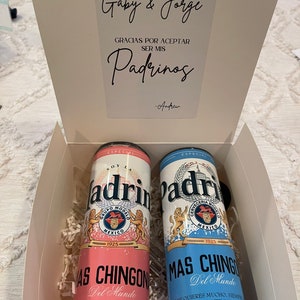 May include: Two pink and blue cans with the words "Soy la Padrino" and "Mas Chingon Del Mundo" on them. The cans are in a white box with a white card that says "Gaby & Jorge Gracias por aceptar ser mis Padrinos -Andrew".