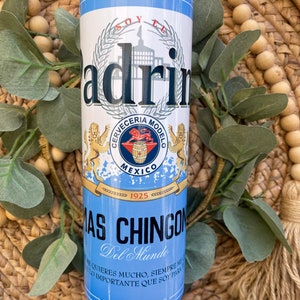 May include: A blue and white insulated tumbler with a graphic of a beer can. The can features the text "Soy El Padrino" and "Cerveceria Modelo" with a lion logo. The text "Mas Chingon Del Mundo" is printed below the can graphic.
