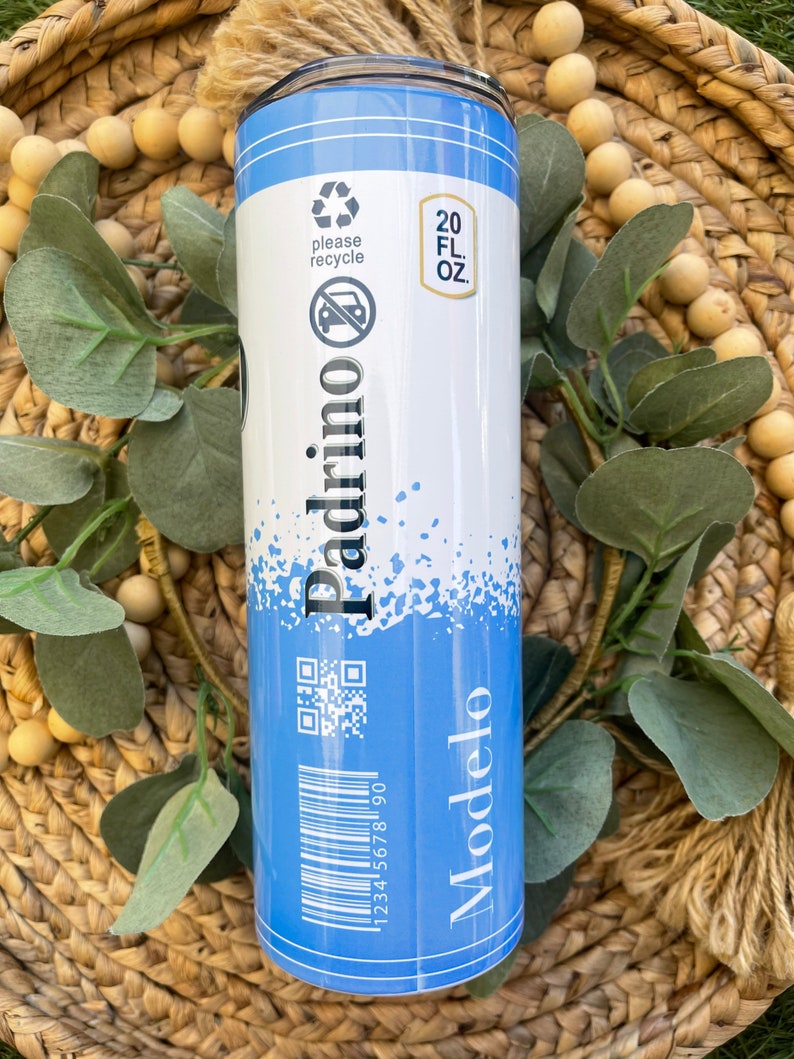 May include: A blue and white 20 fl oz tumbler with a black and white image of a beer bottle and the text "Modelo" and "Padrino". The tumbler has a recycle symbol and a no car symbol. It also has a barcode and a QR code.