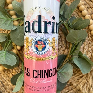 May include: Pink and white insulated tumbler with a graphic of a beer can. The can has the text "Soy La Madrin" and "Grupo Modelo" with a lion logo. The text "Especial" is at the top of the can and "Brewed in Mexico" is at the bottom.