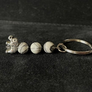 May include: A silver-toned elephant charm keychain with three white and gray patterned beads. The keychain has a silver split ring for attaching keys. The elephant charm is detailed and the beads are smooth and round.