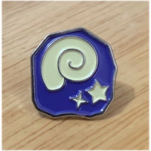 May include: A purple and silver enamel pin with a white seashell and two white stars. The pin is shaped like a rock.