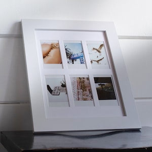 May include: A white picture frame with six small photo openings. The photos inside depict beach scenes, including seagulls, a motel sign, and a bikini. The frame is leaning against a white wall.