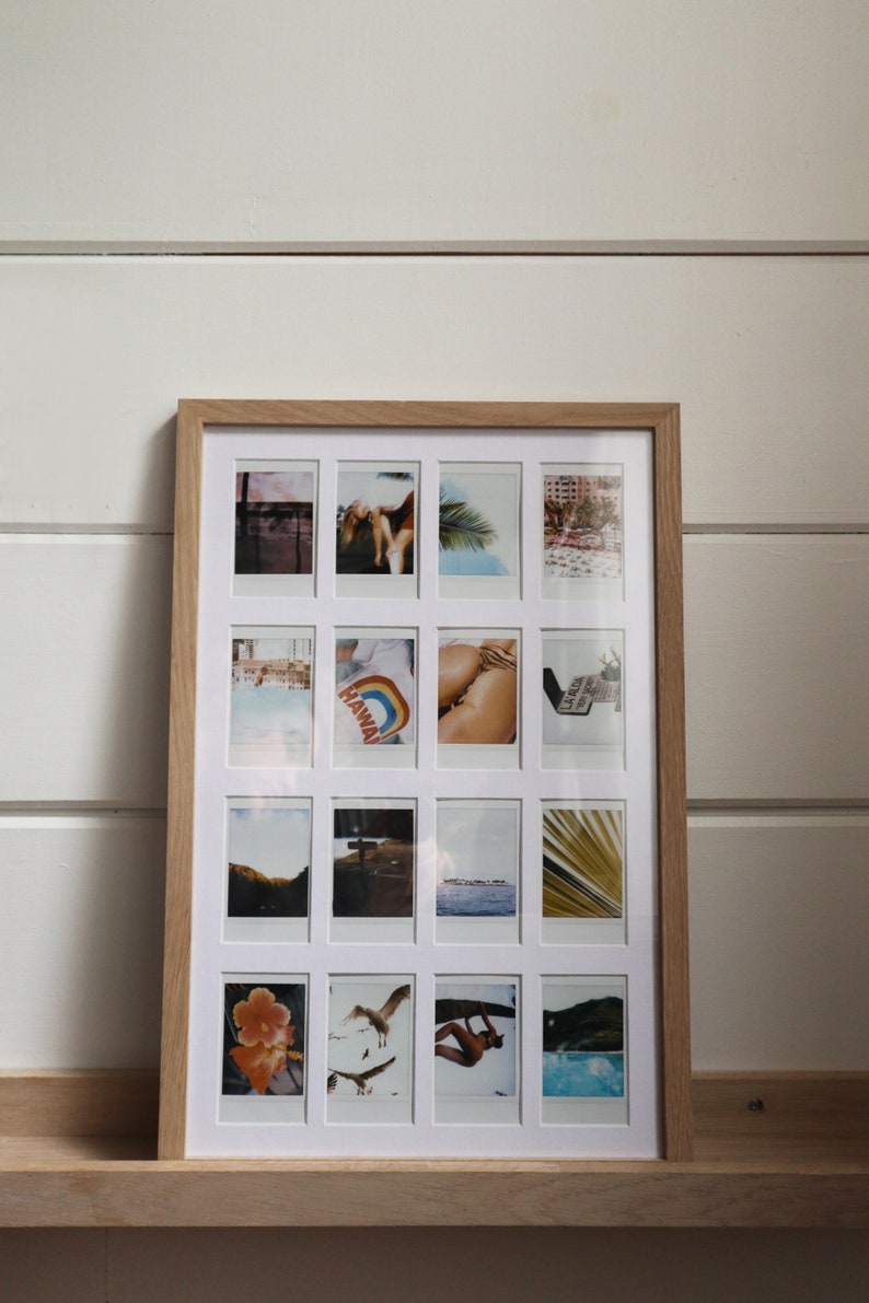 May include: A wooden frame with a white mat holding 16 Polaroid photos. The photos are arranged in a grid pattern and feature a variety of subjects, including landscapes, people, and objects. The frame is on a wooden shelf.