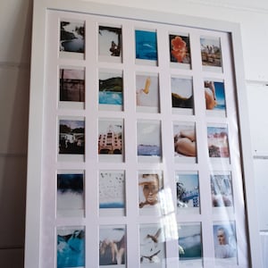 May include: A white picture frame with a collage of 20 Polaroid photos. The photos are arranged in a grid pattern and feature a variety of subjects, including landscapes, people, and objects. The frame is made of wood and has a white finish.