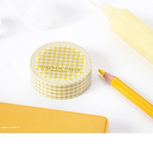 May include: A roll of yellow and white gingham check washi tape. The tape is in a clear plastic dispenser with the words "Gingham Check" printed on the front.