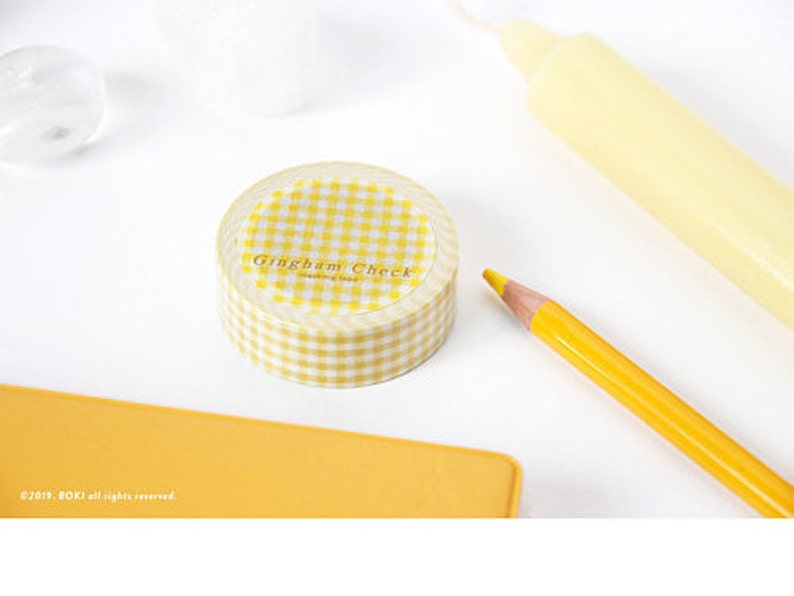 May include: A roll of yellow and white gingham check washi tape. The tape is in a clear plastic dispenser with the words "Gingham Check" printed on the front.