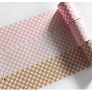 Puede incluir: Tres rollos de cinta washi con un patrón de cuadros. El rollo superior es rosa, el rollo del medio es rosa claro y el rollo inferior es marrón.