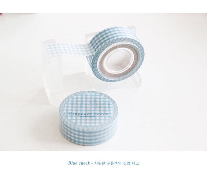 May include: A roll of blue and white gingham patterned washi tape. The tape is on a clear plastic dispenser. The text "Graham Check" is printed on the tape.
