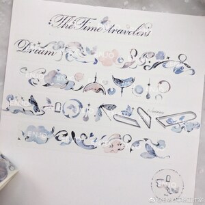 May include: A collection of decorative washi tapes featuring a whimsical watercolour design with clouds, stars, moons, butterflies, and the text "The Time Travelers" and "Dream".