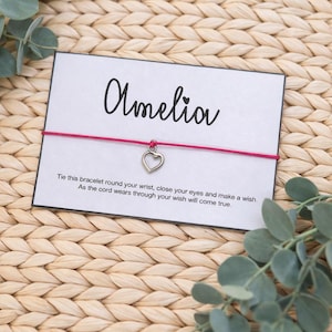 May include: A card with the name "Amelia" in cursive script, a pink cord bracelet with a heart charm, and text that reads "Tie this bracelet round your wrist, close your eyes and make a wish. As the cord wears through your wish will come true."