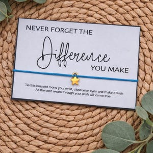 May include: A blue string bracelet with a gold star charm, presented on a white card with the text "NEVER FORGET THE Difference YOU MAKE". The card also includes instructions. The background is a woven texture.