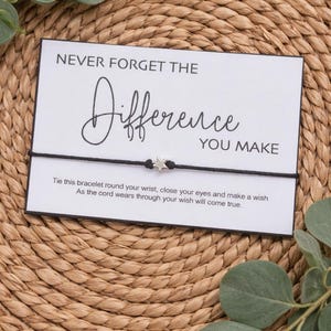 May include: A black cord bracelet with a small silver star charm, displayed on a white card. The card reads "NEVER FORGET THE Difference YOU MAKE" in elegant script. The card also includes instructions.