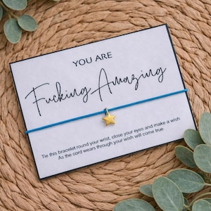 May include: A card with the words "YOU ARE Fucking Amazing" and a blue string bracelet with a gold star charm. The card also includes the text "Tie this bracelet round your wrist, close your eyes and make a wish. As the cord wears through your wish will come true."