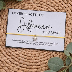 May include: A yellow string bracelet with a silver star charm, presented on a white card with the text "NEVER FORGET THE Difference YOU MAKE". The card includes a message about making a wish. The background is a woven texture.