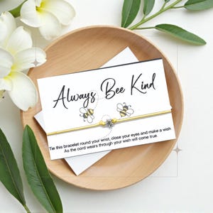 Puede incluir: Un brazalete de cuerda amarillo con dos abalorios de abeja y un abalorio de estrella plateada. El brazalete viene con una tarjeta que dice "Always Bee Kind" e instrucciones sobre cómo hacer un deseo.