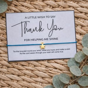 May include: A card with the text "Thank You" and a blue string bracelet with a gold star charm. The card reads "A little wish to say Thank You for helping me shine."