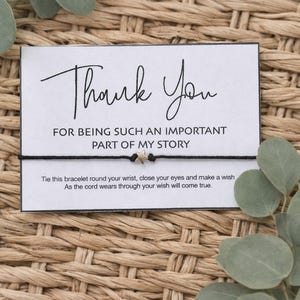 May include: A black cord bracelet with a small star charm, presented on a card that reads "Thank You" in elegant script. The card also includes the text "FOR BEING SUCH AN IMPORTANT PART OF MY STORY."