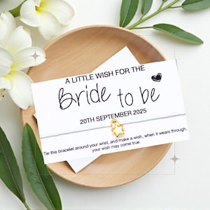 May include: A white card with the text "A Little Wish For The Bride To Be" and the date "20th September 2025". A white string bracelet with a gold star charm is attached to the card.