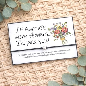 May include: A card with the message "If Auntie's were flowers... I'd pick you!" and a floral illustration. A black cord bracelet with a star charm is in front of the card. The background is a woven pattern.