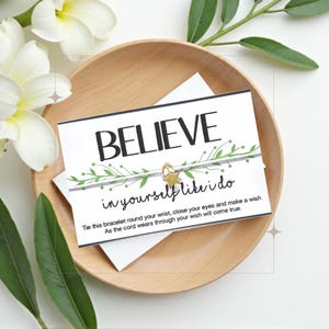 May include: White card with green leaves and a gold star charm on a white string bracelet. The card reads "BELIEVE in yourself like I do". Tie this bracelet round your wrist, close your eyes and make a wish. As the cord wears through your wish will come true.