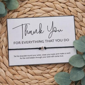 May include: A black cord bracelet with a silver star charm is displayed on a white card with the words "Thank You" and "FOR EVERYTHING THAT YOU DO". The card is on a woven background with green leaves.