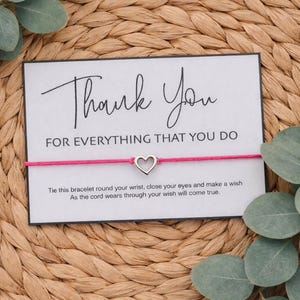 May include: A card with the words "Thank You" and "FOR EVERYTHING THAT YOU DO" printed in black. A pink cord bracelet with a silver heart charm is attached. The card includes instructions. The background is woven.
