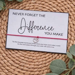 May include: A card with the text "NEVER FORGET THE Difference YOU MAKE" and a red string bracelet with a heart charm. The card includes instructions to tie the bracelet and make a wish.