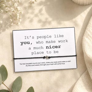 Peut inclure: Un bracelet en cordon noir avec un petit charme en forme d'étoile est présenté sur une carte blanche. La carte indique : « C'est grâce à des gens comme vous que le travail est un endroit beaucoup plus agréable. »