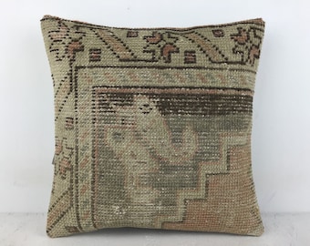 May include: A square throw pillow with a vintage, hand-woven design. The pillow features a geometric pattern in shades of brown, beige, and pink.