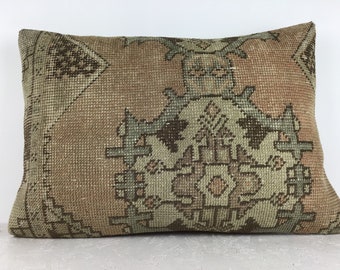 Può includere: Un cuscino decorativo con un motivo marrone, verde e beige. Il cuscino è realizzato in tessuto tessuto e ha una forma rettangolare.