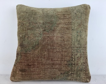May include: A square, green and brown throw pillow with a woven texture. The pillow is made from a vintage rug.