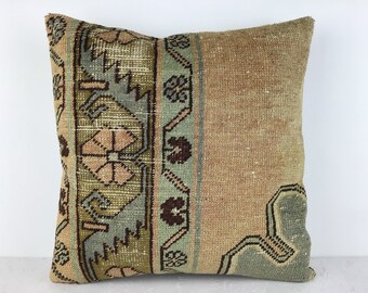 May include: A decorative pillow with a green, brown, and beige patterned design. The pillow has a woven texture and a fringed edge.
