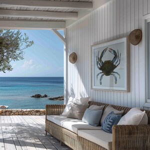 May include: A wicker sofa with white cushions sits on a wooden deck overlooking a blue ocean. A framed print of a blue crab hangs on the white wall behind the sofa.