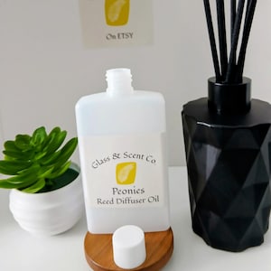 May include: A black geometric glass reed diffuser bottle with black reeds, a white plastic bottle of Peonies Reed Diffuser Oil with a white cap, and a small green succulent in a white pot. A logo for Glass & Scent Co. is visible on the label.