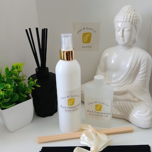 May include: A white room spray bottle with a gold cap, a clear reed diffuser oil bottle, a black geometric diffuser vessel with black reeds, a white Buddha statue, and two bundles of reeds tied with a cream ribbon, all labelled Glass & Scent Co.