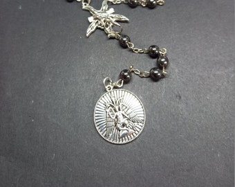 May include: A black hematite rosary with a silver angel pendant. The rosary has a silver crucifix with a detailed design.