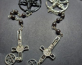 May include: Two rosary necklaces with dark brown beads and silver-tone metal pendants. One necklace features a black pentagram pendant with a goat head, and the other has a silver pentagram pendant. Both have a cross pendant with a pentagram charm.