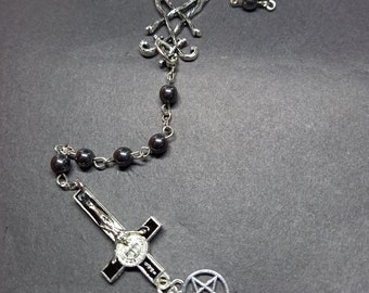 May include: A black rosary necklace with a silver crucifix and a pentagram pendant. The crucifix has a black background and a silver image of Jesus.