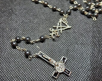 May include: A beaded necklace featuring dark, polished spherical beads linked by silver-toned metal chains. The design includes several small silver pentagram charms and a central silver-toned inverted cross pendant with a black inlay and a circular emblem.