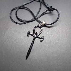 May include: A black ankh pendant necklace with a black cord. The ankh is a symbol of life in ancient Egypt.