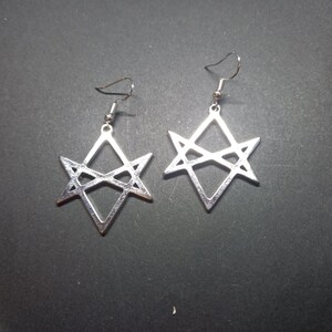 May include: A pair of silver-toned metal earrings featuring a geometric star design. Each earring consists of a six-pointed star shape formed by intersecting triangles, suspended from a standard silver-colored metal fishhook ear wire.