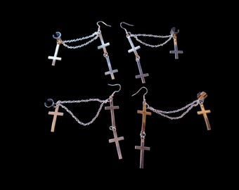 May include: A set of four silver cross earrings with chains. Each earring has three cross charms and a clip-on ear cuff.
