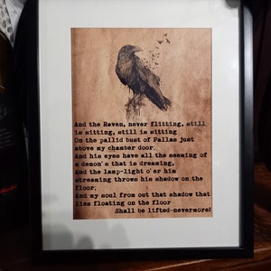 May include: Framed print featuring a detailed illustration of a raven perched on a branch, with text from a poem below. The artwork is set against a sepia-toned background, framed in black.