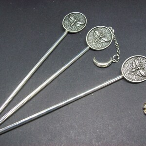 May include: Three silver hair sticks with decorative metal tops. One stick has a crescent moon charm and a skull charm. The other two sticks have a butterfly design.