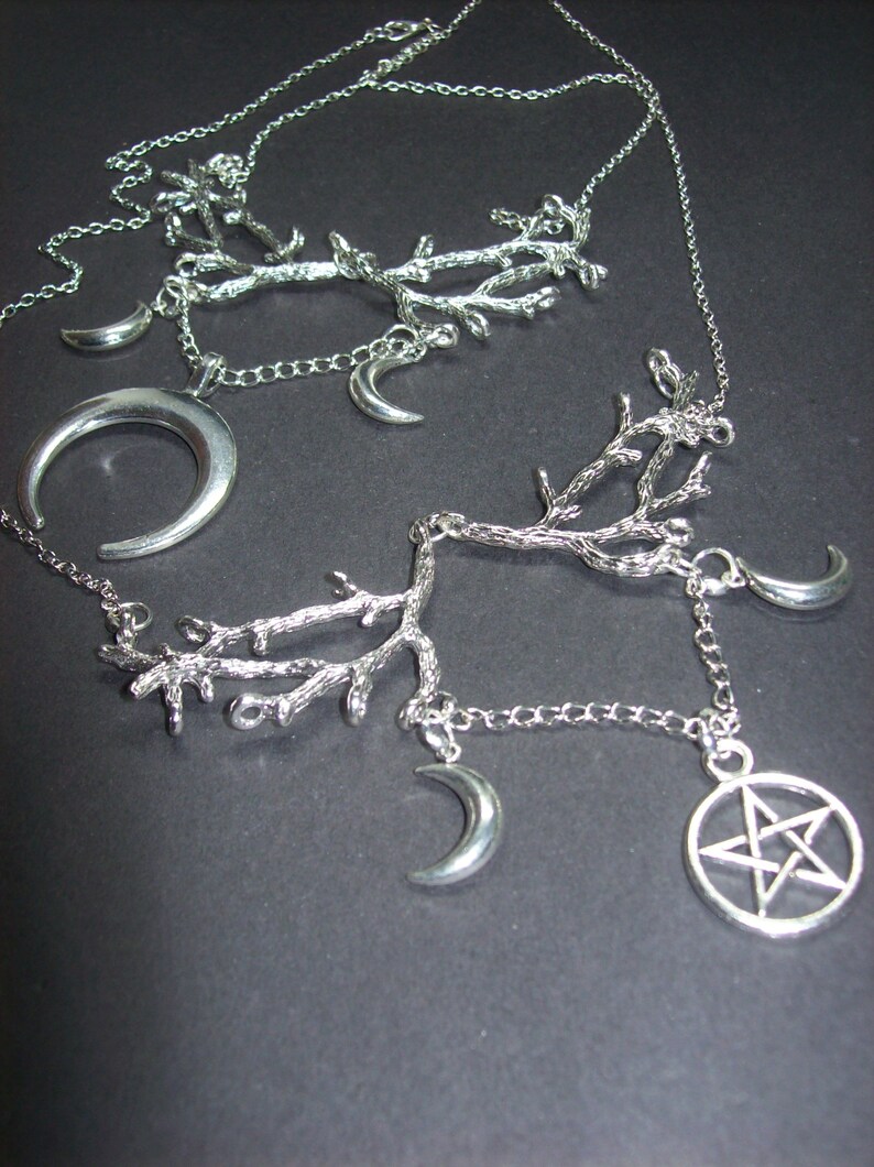 May include: Silver-toned necklaces featuring branch-like designs, crescent moons, and a pentagram pendant. The necklaces are displayed against a dark background, showcasing the intricate details of the jewelry.