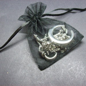 May include: A silver crescent moon pendant necklace and chain inside a small black mesh drawstring bag. The necklace is a delicate piece of jewelry, perfect for everyday wear or special occasions. The bag is closed with a black satin drawstring.